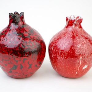 May include: Two red ceramic pomegranate ornaments. One has a black glaze and the other has a white glaze.