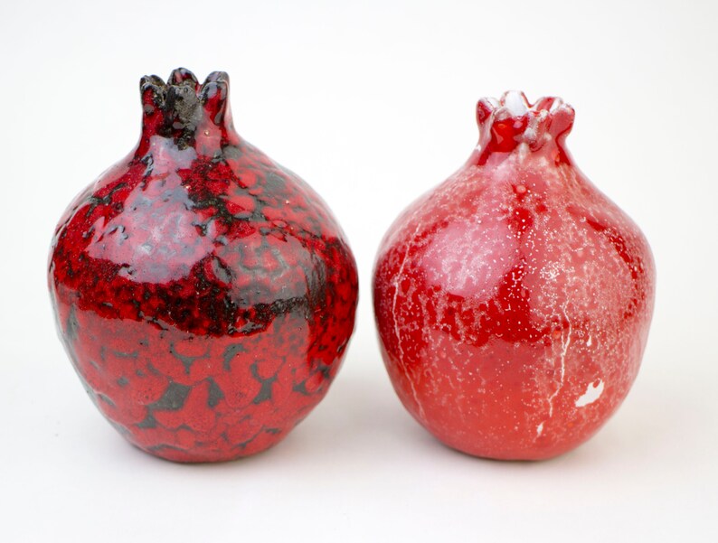 May include: Two red ceramic pomegranate ornaments. One has a black glaze and the other has a white glaze.