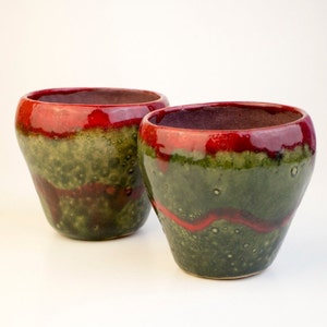 May include: Two ceramic cups with a green and red glaze. The cups are round and have a wide opening.