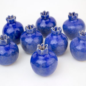 Può includere: Otto piccoli melograni in ceramica blu disposti in cerchio su uno sfondo bianco.