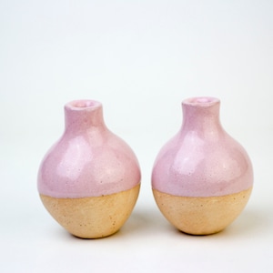 May include: Two small, round ceramic vases with a light pink glaze on the top half and a natural brown glaze on the bottom half.