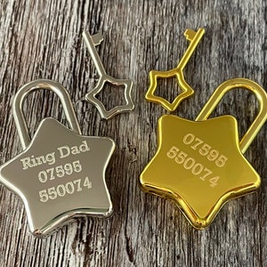 Puede incluir: Dos candados en forma de estrella con llaves. Un candado es plateado y está grabado con "Ring Dad 07595 550074". El otro candado es dorado y está grabado con "07595 550074".