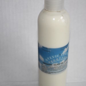 Puede incluir: Una botella de pl&aacute;stico blanca de loci&oacute;n de aceite de oliva org&aacute;nico con una etiqueta azul que dice "Sylvie Clinic" y "Loci&oacute;n de aceite de oliva org&aacute;nico".
