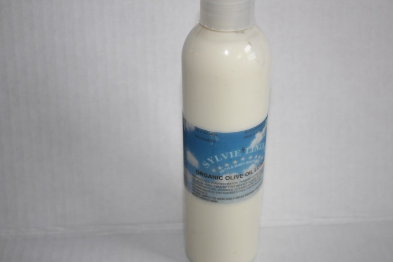 Puede incluir: Una botella de pl&aacute;stico blanca de loci&oacute;n de aceite de oliva org&aacute;nico con una etiqueta azul que dice "Sylvie Lind" y "Loci&oacute;n de aceite de oliva org&aacute;nico".
