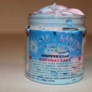 May include: A clear jar of whipped soap with a blue and pink swirl. The label reads "Whipped Soap Birthday Cake" and lists ingredients. The jar is labeled "Linie Bath Body Boutique".