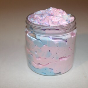 May include: A glass jar filled with a pink and blue swirl whipped body butter. The top of the butter is decorated with glitter.