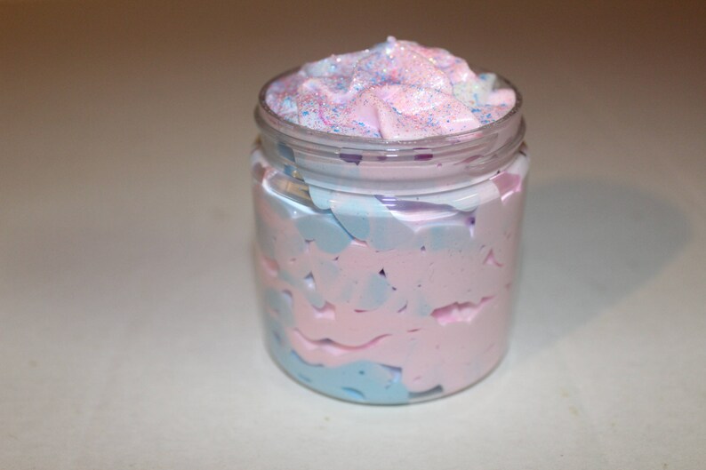 May include: A glass jar filled with a pink and blue swirl whipped body butter. The top of the butter is decorated with glitter.