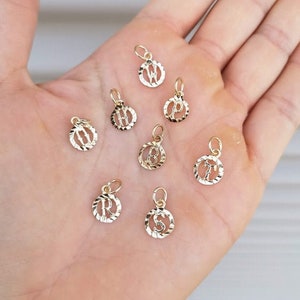 May include: A collection of gold-toned initial letter charms. Each charm is a circle with a raised letter in the center. The letters are W, P, H, B, R, S, and T.