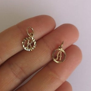 May include: Two gold-colored initial charms, one with the letter "K" and the other with the letter "A", both in a circular design with a textured edge.