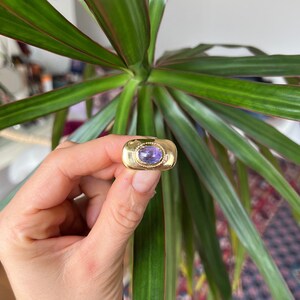 May include: A gold ring with a purple oval gemstone set in a bezel setting.
