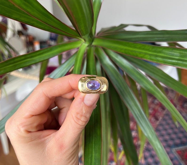 May include: A gold ring with a purple oval gemstone set in a bezel setting.