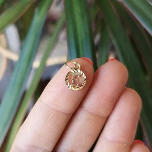 May include: Gold charm with a letter E in a circle. The charm is on a finger.