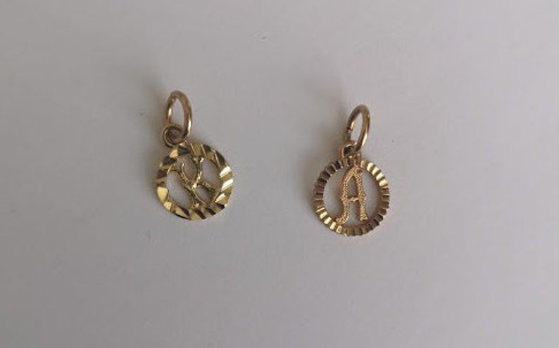 May include: Two gold-colored pendants with a circular design. The pendants feature the letters "R" and "A" in a cutout style.
