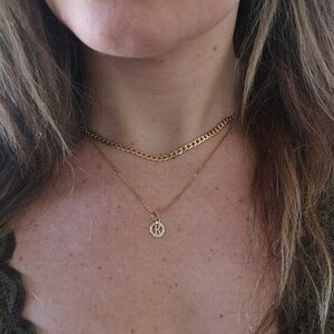 May include: A gold chain necklace with a small pendant featuring the letter K. The necklace is layered over a thicker gold chain.