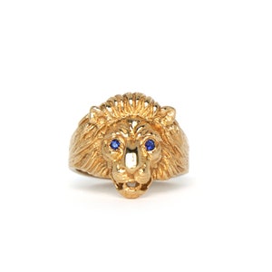 Könnte beinhalten: Ein goldener Löwenkopfring mit blauen Edelsteinaugen.