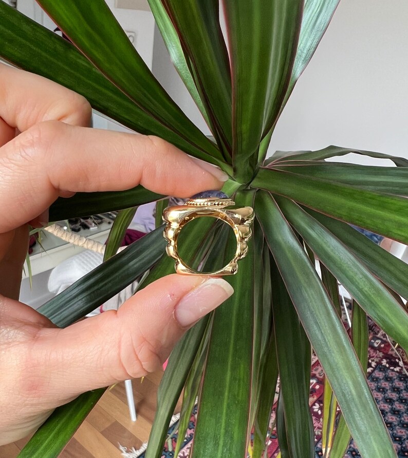 May include: A gold ring with a large, round, blue gemstone set in the center. The ring has a textured, beaded design around the band.