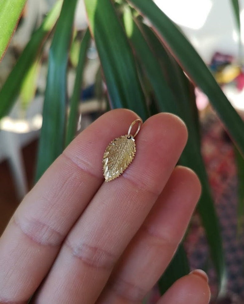 May include: A gold leaf charm pendant. The charm is detailed with a textured design.