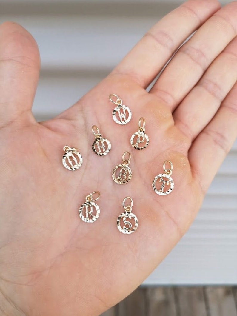 May include: A collection of gold-toned initial letter charms. Each charm is a circle with a raised letter in the center. The letters are W, P, H, B, R, S, and T.