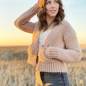 May include: A pink crocheted cardigan with a button closure and pockets. The cardigan is cropped and has a ribbed hem and cuffs.
