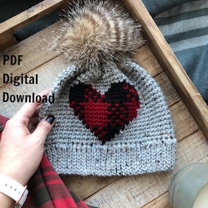 May include: A gray crochet beanie with a red and black heart design and a fluffy brown pom pom. The beanie is sitting on a wooden surface. PDF Digital Download.