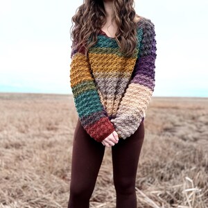 May include: A woman wearing a multi-coloured striped crochet sweater with brown leggings and white socks with colourful stripes.