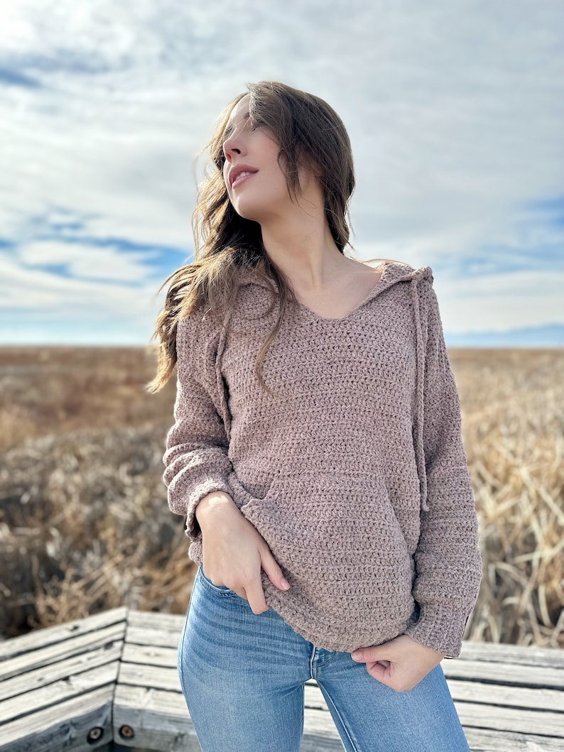 May include: A brown crocheted hooded sweater with a relaxed fit. The sweater has a V-neck and a drawstring hood.