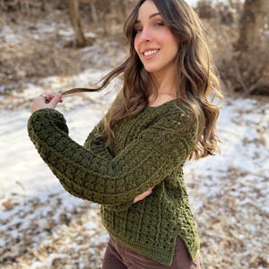 Puede incluir: Un suéter de crochet verde de corte holgado y ligeramente más largo en la espalda. El suéter tiene un patrón de punto texturizado y una abertura lateral en el lado derecho.