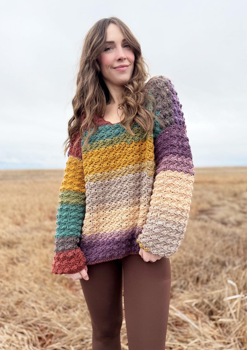 May include: A multi-coloured striped crochet sweater with a v-neck and long sleeves. The sweater is made with a textured stitch and has a relaxed fit.