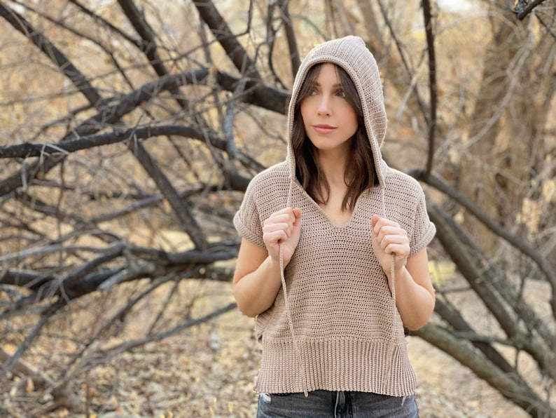 May include: A light brown crocheted hooded top with short sleeves and a v-neck.