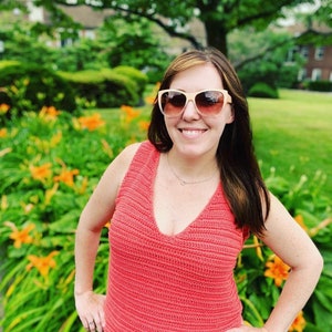 May include: A woman wearing a coral crochet tank top with a deep V-neckline. She is wearing sunglasses and smiling.
