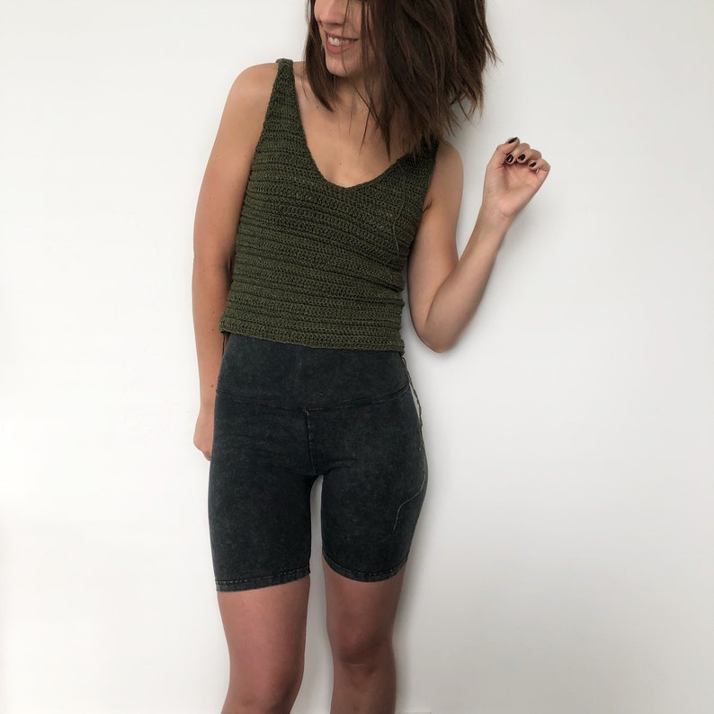 May include: A woman wearing a green crochet tank top and black biker shorts.