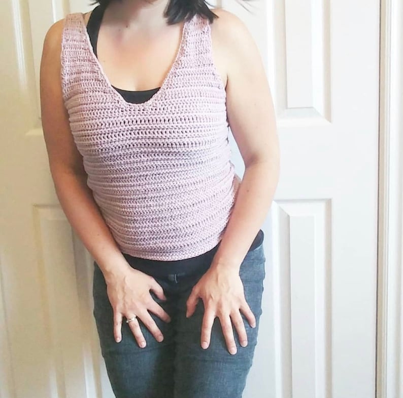May include: A pink crocheted tank top with a v-neckline. The tank top is made with a simple stitch pattern and has a relaxed fit.