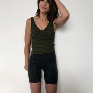 May include: A woman wearing a green crochet tank top and black biker shorts.