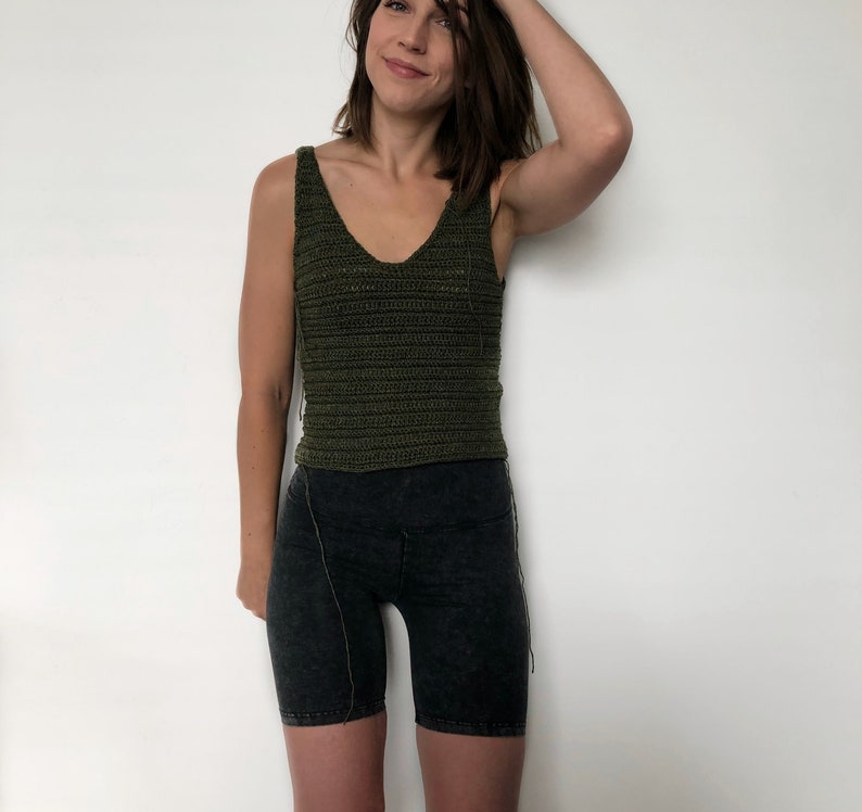 May include: A woman wearing a green crochet tank top and black biker shorts.