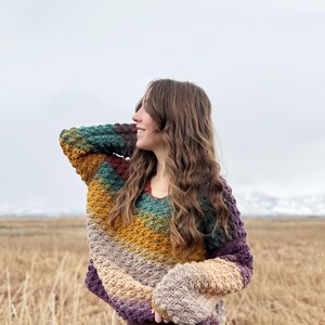 May include: A multi-coloured crocheted sweater with a v-neck and long sleeves. The sweater is made in a variety of shades of brown, purple, green, and yellow.