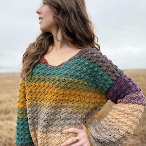 May include: A multi-coloured crochet sweater with a v-neck and long sleeves. The sweater is made with a textured stitch and features stripes of rust, mustard yellow, beige, teal, and purple.