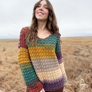 May include: A multi-coloured striped crochet sweater with long sleeves. The sweater is made with a textured stitch and features a variety of colours, including rust, teal, mustard yellow, beige, and purple.