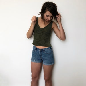 May include: A woman wearing a green crochet tank top and blue denim shorts.