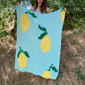 Puede incluir: Una manta de ganchillo con fondo azul claro y limones amarillos con hojas verdes.