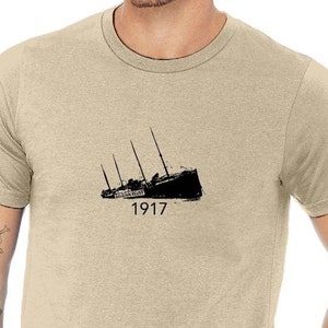 May include: A beige t-shirt with a black silhouette of the Titanic sinking with the year 1917 printed below the image.