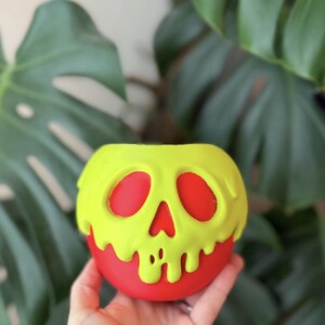 Op de afbeelding: Een ronde, appelvormige houder met een fel limoengroene schedelopzetstuk met een druipend effect. De schedel heeft twee grote ovale oogkassen en een driehoekige neusholte, waardoor de effen rode basiskleur eronder zichtbaar wordt.