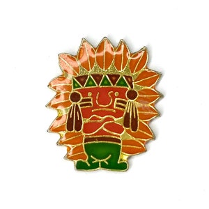 May include: A colorful enamel pin featuring a Native American chief design. The pin has a red face, orange headdress, and green base, with gold-colored accents. The design is detailed and eye-catching, perfect for adding a unique touch to any outfit.