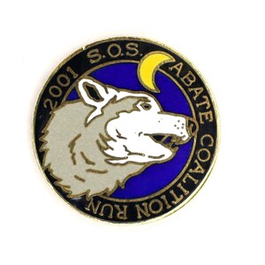 May include: A black and gold circular pin with a white wolf howling at a yellow crescent moon on a blue background. The text "2001 S.O.S. ABATE COALITION RUN" is written around the edge of the pin.