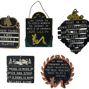 May include: A collection of vintage metal signs with humorous sayings. The signs are in various shapes and sizes, featuring text like "Where There's a Will There's a Relative" and "Come In, Sit Down, Relax, Converse."