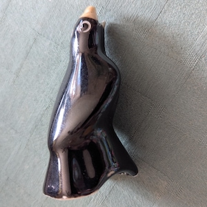 May include: A glossy black ceramic penguin figurine with a light tan beak and eye detail. The penguin has a sleek, curved body and a small, upturned tail. The figurine is a decorative item.