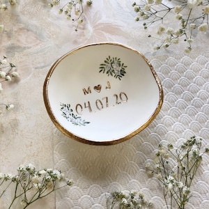 Puede incluir: Plato de cer&aacute;mica blanca para anillos con borde dorado y dise&ntilde;o floral. El plato est&aacute; personalizado con las iniciales "M & J" y la fecha "04.07.20".