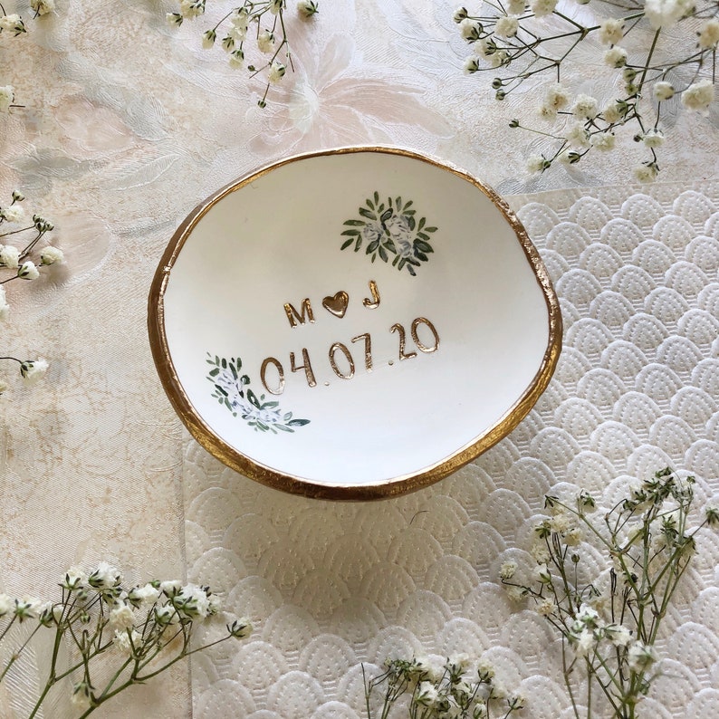 Puede incluir: Plato de cer&aacute;mica blanca para anillos con borde dorado y dise&ntilde;o floral. El plato est&aacute; personalizado con las iniciales "M & J" y la fecha "04.07.20".