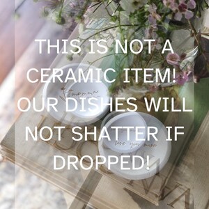 K&ouml;nnte beinhalten: Zwei wei&szlig;e Keramik-Schalen mit handgeschriebenen Botschaften, "Momma" und "Love you more", auf einem Stapel B&uuml;cher. Der Text "This is not a ceramic item! Our dishes will not shatter if dropped!" ist auf dem Bild zu sehen.
