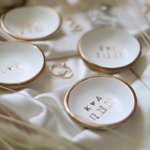 May include: Four white ceramic ring dishes with gold trim. Each dish has a different inscription in gold lettering. The inscriptions are "LOVE", "BOY & GIRL", "K & A 12.28.23", and "12.28.23".
