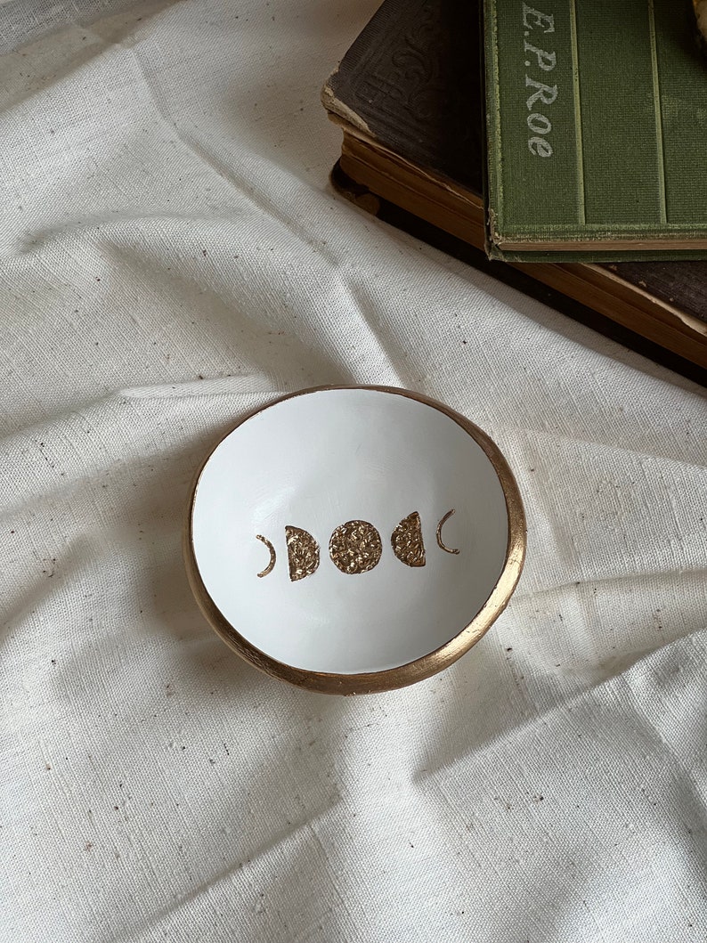 K&ouml;nnte beinhalten: Wei&szlig;e Keramik-Ring Schale mit goldfarbenem Rand und einem goldenen Mondphasen-Design.